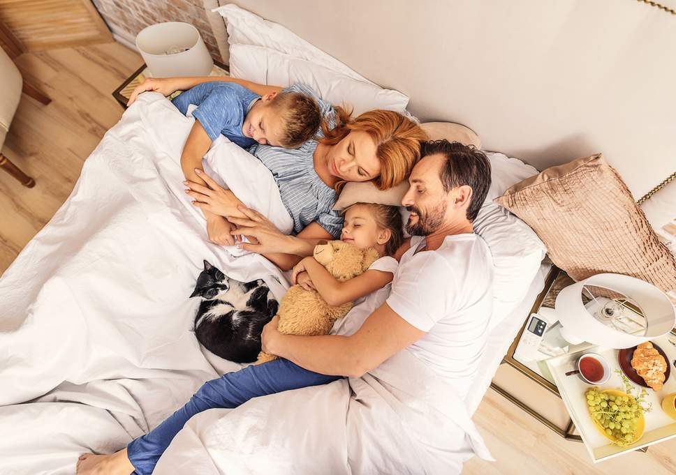 family and cat sleeping on bed
